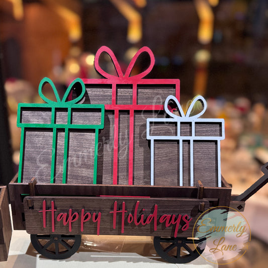A decorative shelf sitter kit featuring a wooden wagon with 'Happy Holidays' text, adorned with green and red presents, and a happy holidays banner.