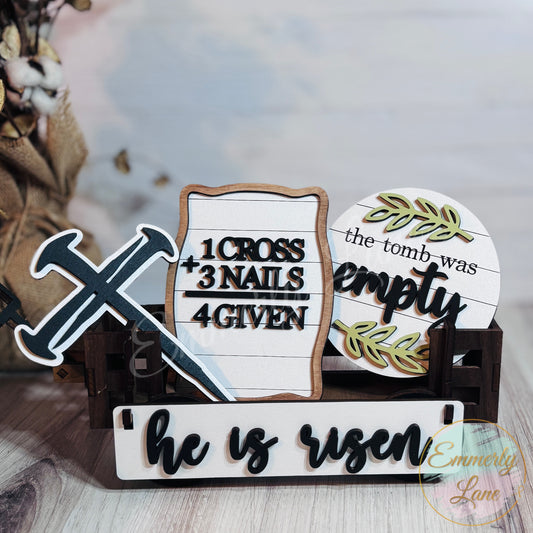 A handcrafted Easter shelf sitter kit made from maple plywood with phrases 'He Is Risen' and 'The Tomb Was Empty' painted on it, displayed in a wagon.