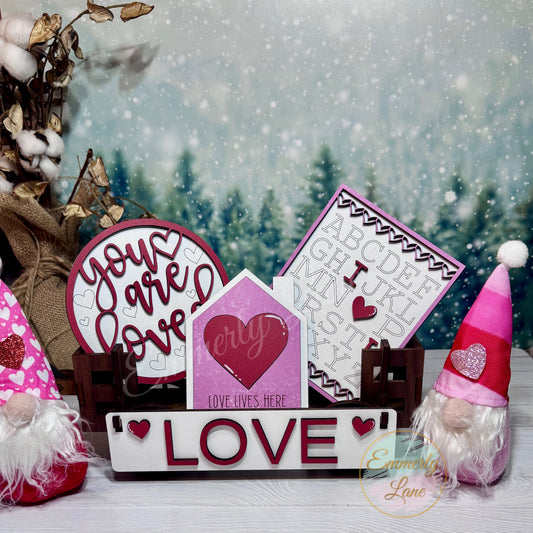 A shelf sitter kit with a 'Love' theme, including a heart-shaped sign, a 'Love' banner, and other decorative elements, displayed against a wintry backdrop.